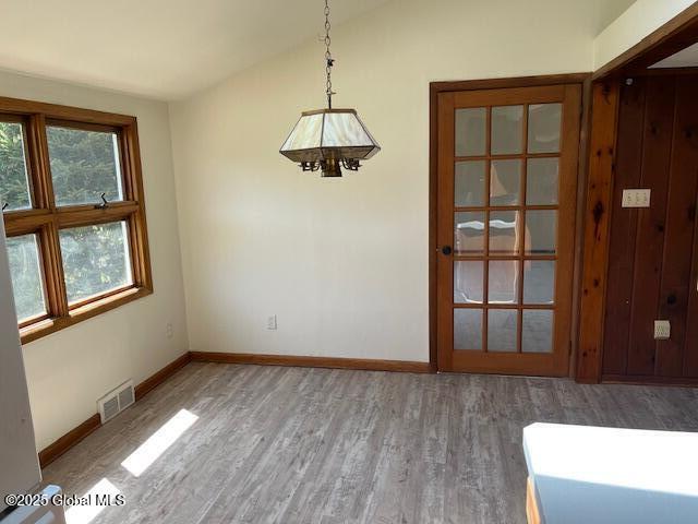 unfurnished dining area with visible vents, vaulted ceiling, wood finished floors, baseboards, and a notable chandelier