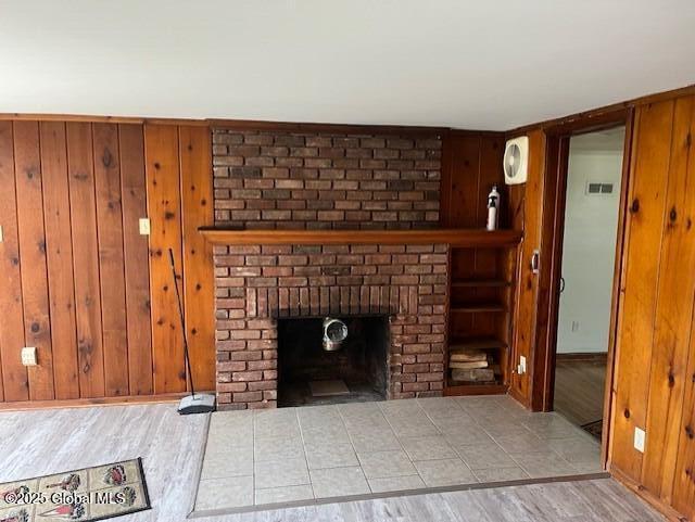 unfurnished living room with a brick fireplace, wooden walls, visible vents, and wood finished floors