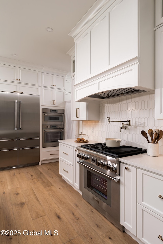 kitchen featuring premium range hood, tasteful backsplash, white cabinets, high end appliances, and light hardwood / wood-style floors