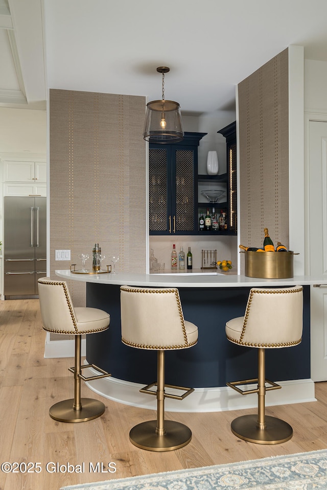 bar with built in refrigerator, hanging light fixtures, and light hardwood / wood-style flooring