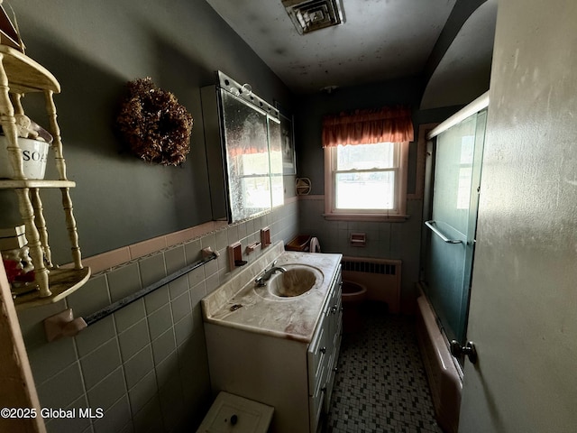 full bathroom featuring radiator heating unit, vanity, bath / shower combo with glass door, tile walls, and toilet