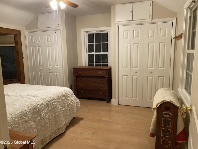 bedroom featuring two closets, light hardwood / wood-style flooring, ceiling fan, and vaulted ceiling