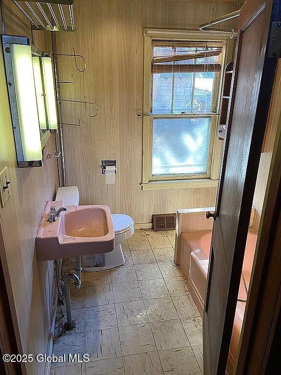 bathroom with a tub to relax in, wooden walls, sink, and toilet