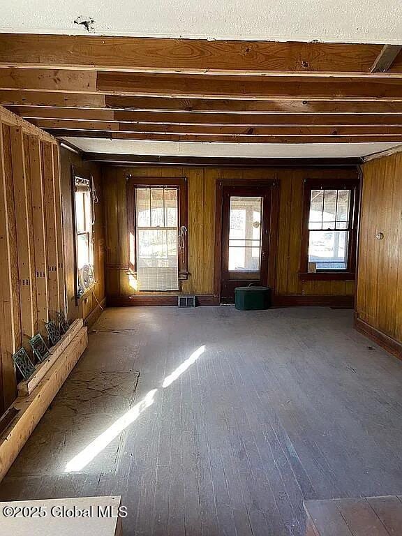 interior space with beamed ceiling, wooden walls, and hardwood / wood-style floors