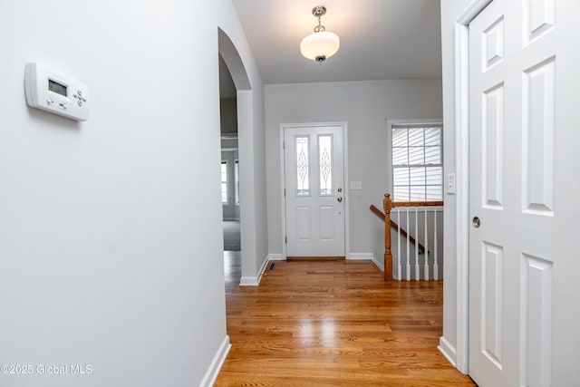 entryway featuring arched walkways, light wood-type flooring, and baseboards