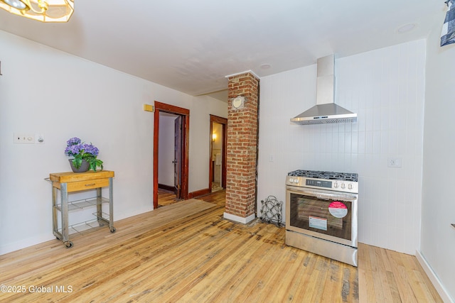 kitchen with decorative columns, stainless steel gas range oven, wall chimney range hood, and light hardwood / wood-style floors