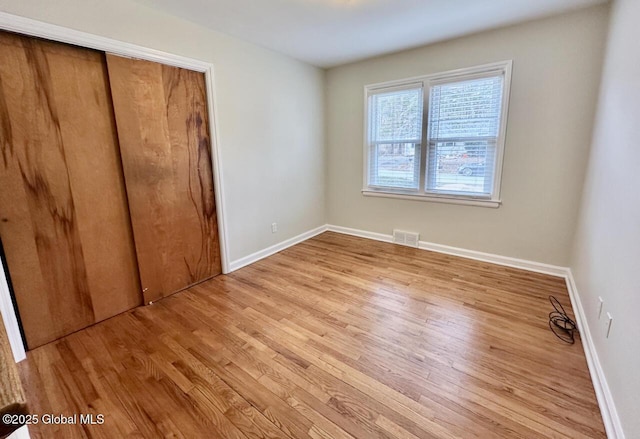 unfurnished bedroom with wood finished floors, visible vents, a closet, and baseboards