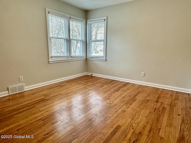 empty room with wood finished floors, visible vents, and baseboards