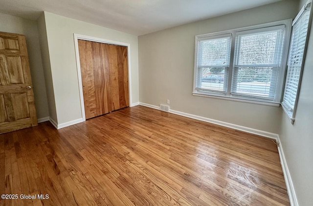 unfurnished bedroom with a closet, baseboards, visible vents, and wood finished floors