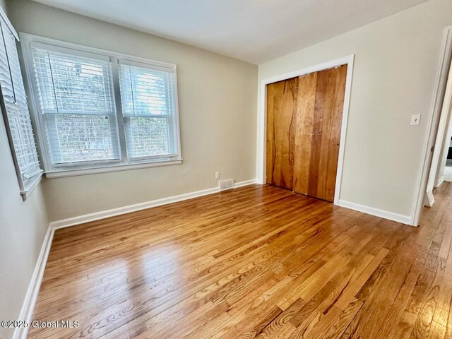 unfurnished bedroom featuring a closet, baseboards, visible vents, and wood finished floors