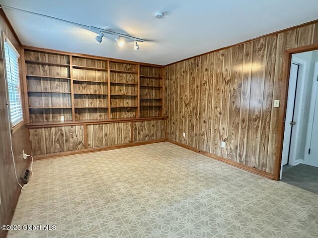 spare room featuring wood walls, rail lighting, and baseboards