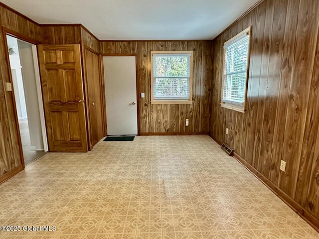 spare room with crown molding, light floors, visible vents, and wood walls