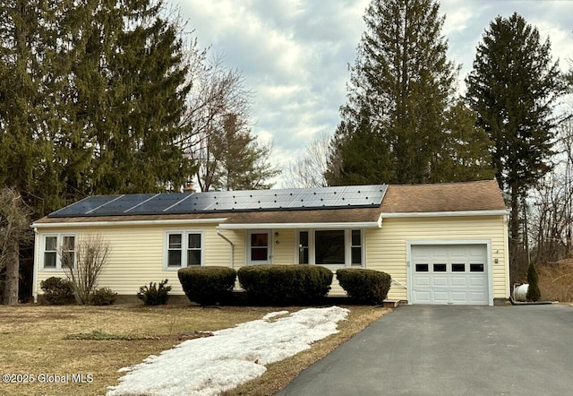 ranch-style house featuring a garage, roof mounted solar panels, and aphalt driveway