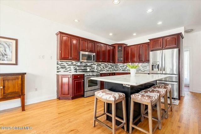 kitchen featuring stainless steel appliances, a kitchen breakfast bar, tasteful backsplash, light hardwood / wood-style floors, and a kitchen island