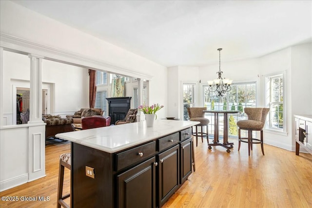 kitchen featuring a breakfast bar area, light hardwood / wood-style flooring, dark brown cabinetry, decorative light fixtures, and ornate columns