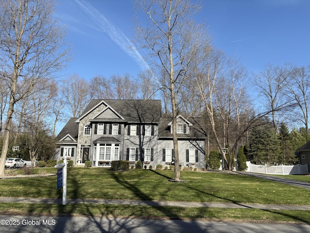 colonial inspired home featuring roof with shingles, a front lawn, and fence