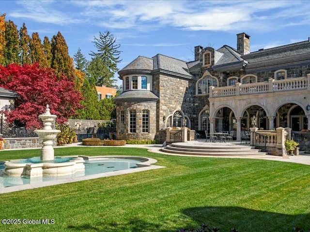 back of house featuring a lawn, a patio, a balcony, stone siding, and a fireplace