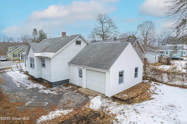 view of snow covered exterior with a chimney, a shingled roof, aphalt driveway, and a garage