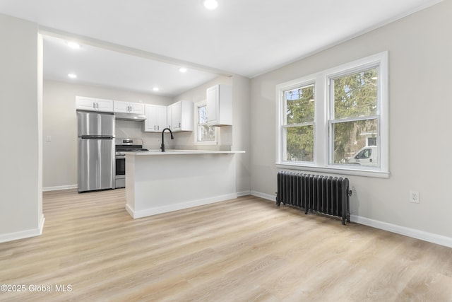 kitchen featuring radiator, a peninsula, light wood-style flooring, stainless steel appliances, and white cabinets