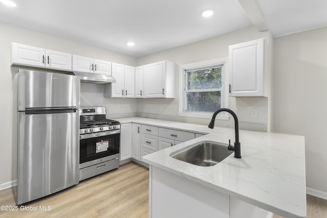 kitchen with light stone countertops, under cabinet range hood, appliances with stainless steel finishes, a peninsula, and a sink