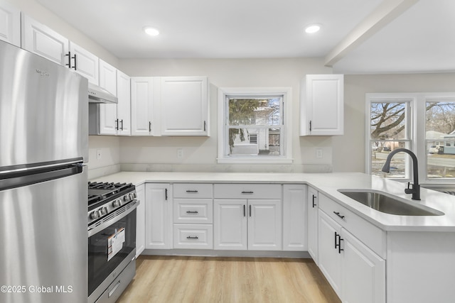 kitchen featuring under cabinet range hood, light wood-type flooring, light countertops, stainless steel appliances, and a sink