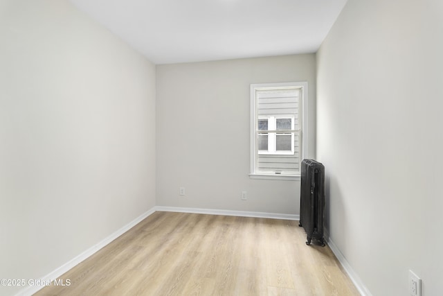 empty room with baseboards, radiator heating unit, and light wood finished floors