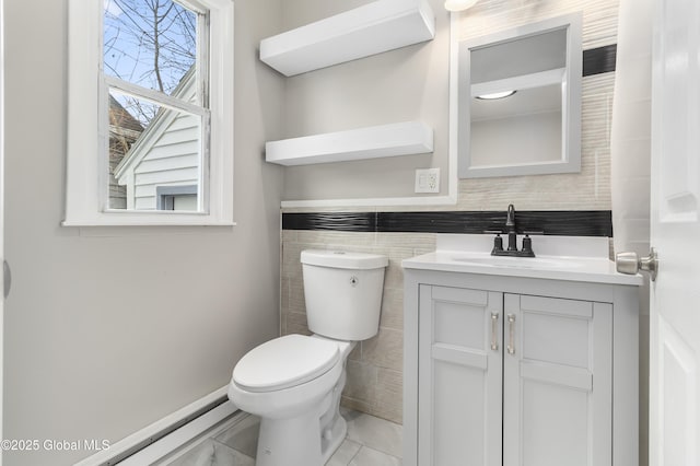 half bath with toilet, tile walls, vanity, and a baseboard radiator