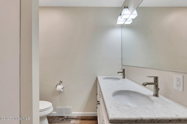 bathroom featuring double vanity, visible vents, toilet, and a sink