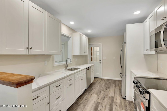 kitchen with light wood-style flooring, a sink, light stone counters, white cabinetry, and stainless steel appliances