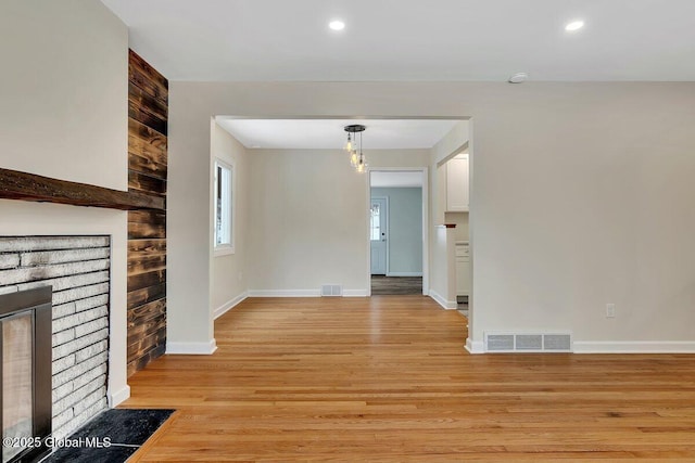 unfurnished living room featuring visible vents, baseboards, a brick fireplace, and light wood finished floors