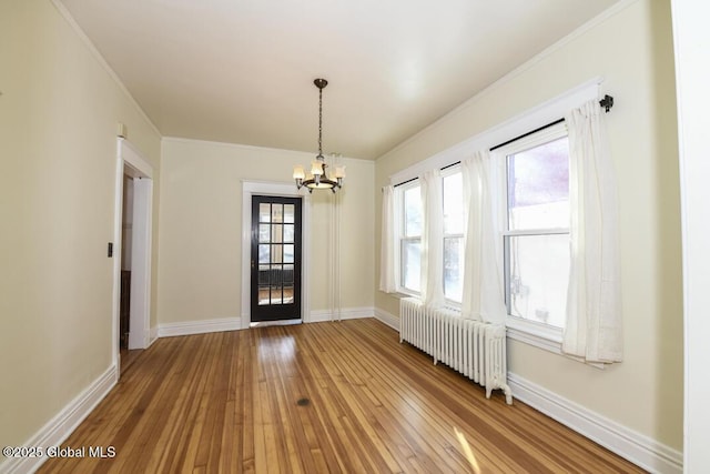 unfurnished dining area featuring hardwood / wood-style flooring, ornamental molding, radiator heating unit, and an inviting chandelier