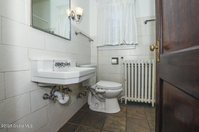 bathroom featuring radiator heating unit, toilet, sink, and tile walls