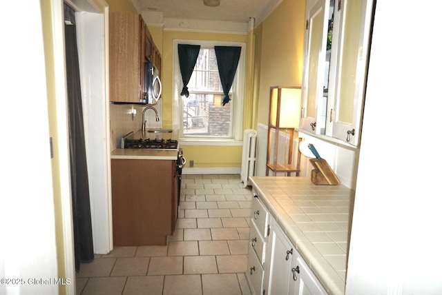 kitchen featuring light tile patterned flooring, radiator, sink, white cabinets, and tile counters