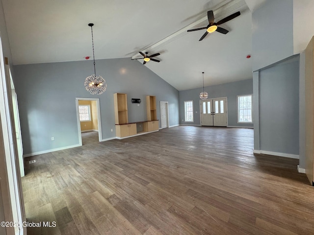 unfurnished living room with dark hardwood / wood-style flooring, ceiling fan with notable chandelier, and high vaulted ceiling