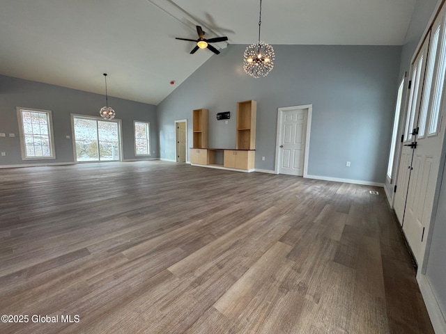 unfurnished living room featuring dark wood-type flooring, ceiling fan with notable chandelier, and high vaulted ceiling