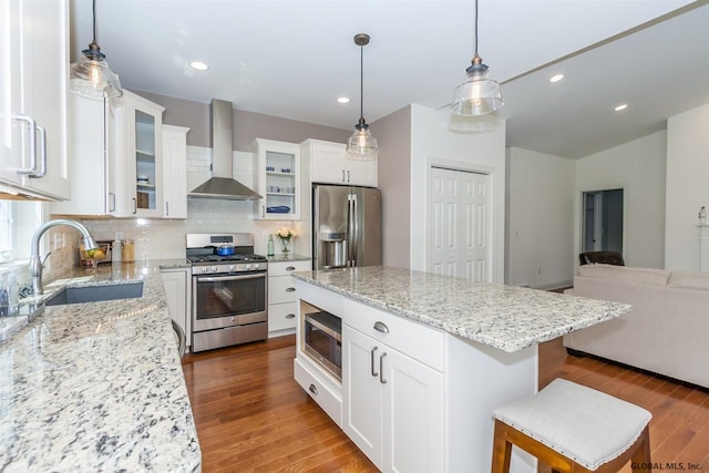 kitchen featuring sink, white cabinets, a kitchen breakfast bar, stainless steel appliances, and wall chimney exhaust hood