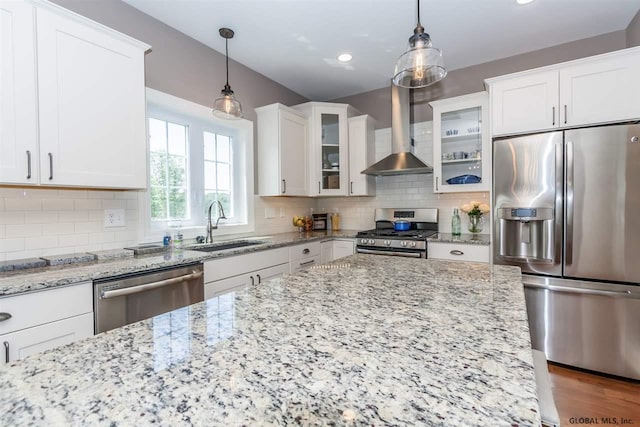 kitchen featuring wall chimney range hood, sink, stainless steel appliances, and hanging light fixtures