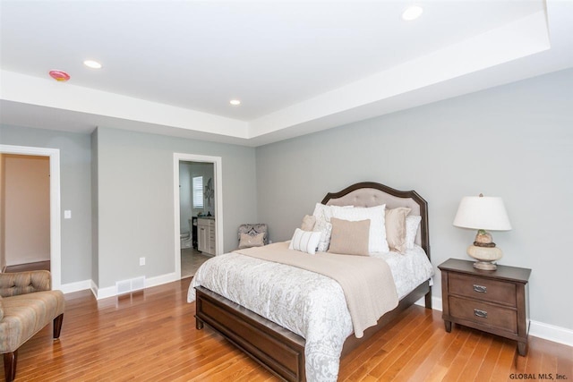 bedroom featuring a tray ceiling, connected bathroom, and light wood-type flooring