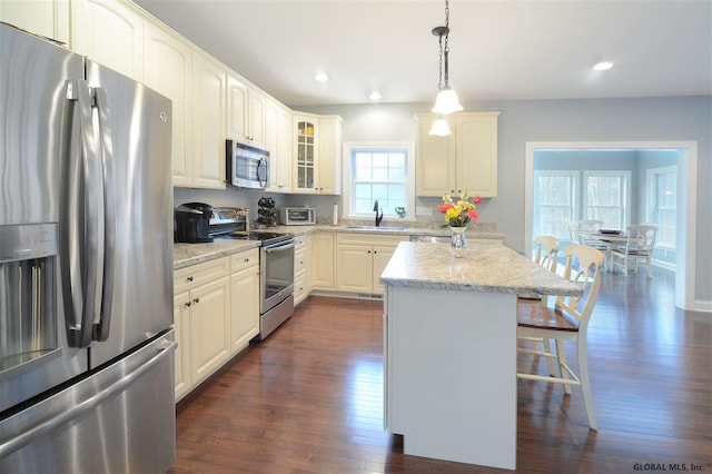 kitchen with light stone counters, decorative light fixtures, appliances with stainless steel finishes, dark hardwood / wood-style floors, and a kitchen island