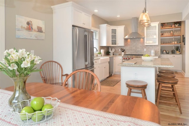 kitchen with white cabinetry, stainless steel appliances, decorative light fixtures, and wall chimney range hood