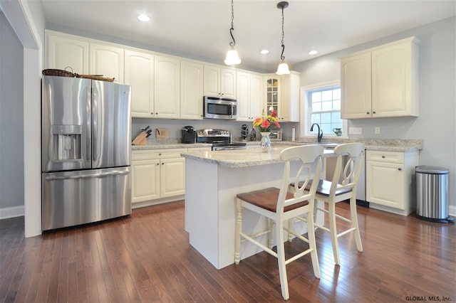 kitchen with appliances with stainless steel finishes, hanging light fixtures, a center island, light stone countertops, and dark hardwood / wood-style flooring