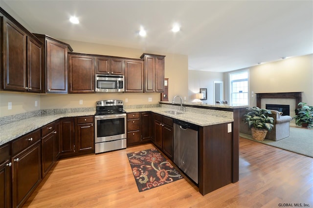 kitchen with sink, stainless steel appliances, dark brown cabinetry, light hardwood / wood-style floors, and kitchen peninsula