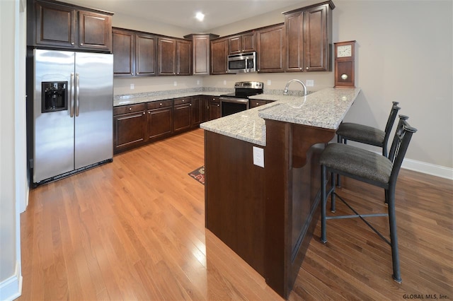 kitchen with dark brown cabinets, a kitchen breakfast bar, stainless steel appliances, kitchen peninsula, and light wood-type flooring