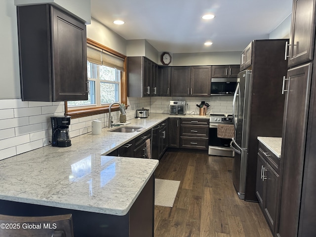 kitchen with sink, dark hardwood / wood-style flooring, light stone counters, kitchen peninsula, and stainless steel appliances