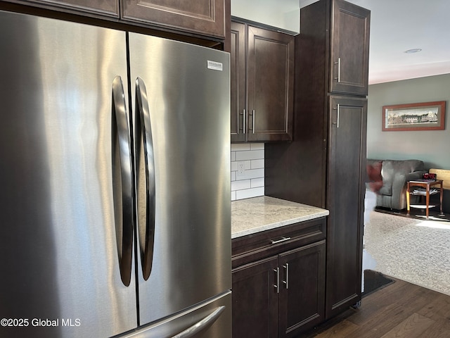 kitchen featuring stainless steel fridge, dark hardwood / wood-style flooring, decorative backsplash, dark brown cabinetry, and light stone countertops