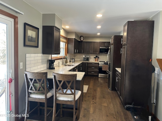 kitchen featuring appliances with stainless steel finishes, dark hardwood / wood-style floors, sink, decorative backsplash, and kitchen peninsula