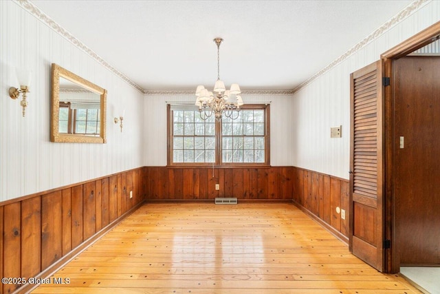 unfurnished dining area featuring an inviting chandelier, light hardwood / wood-style flooring, and wood walls