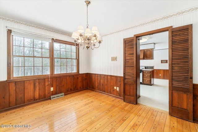 unfurnished room featuring a notable chandelier, wooden walls, and light hardwood / wood-style floors