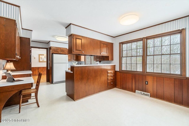 kitchen featuring white refrigerator, ornamental molding, wooden walls, and kitchen peninsula