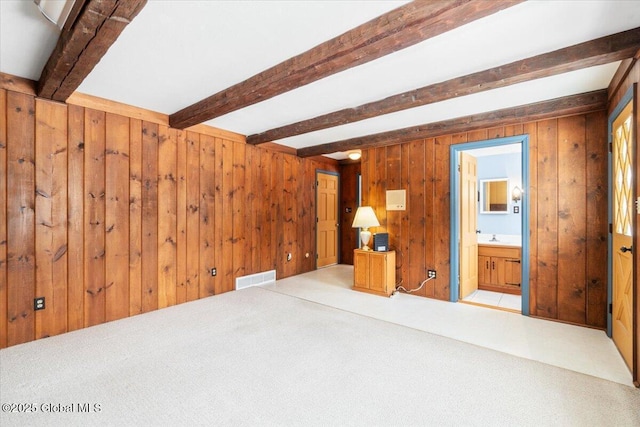 unfurnished room featuring light carpet, sink, beamed ceiling, and wood walls